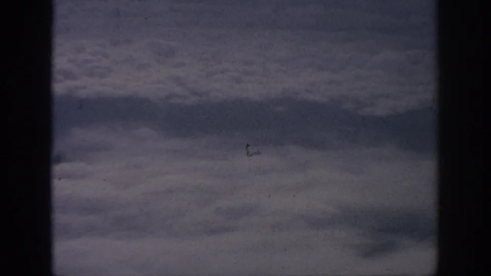 1962 8mm passenger-window shot of a wide cloud deck, framed by dark aircraft-window edges and subtle film wear.