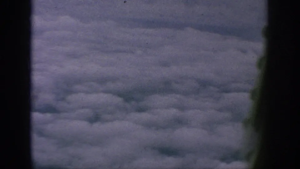 1962 archival home-movie frame looking from an airplane window across a broad layer of clouds.