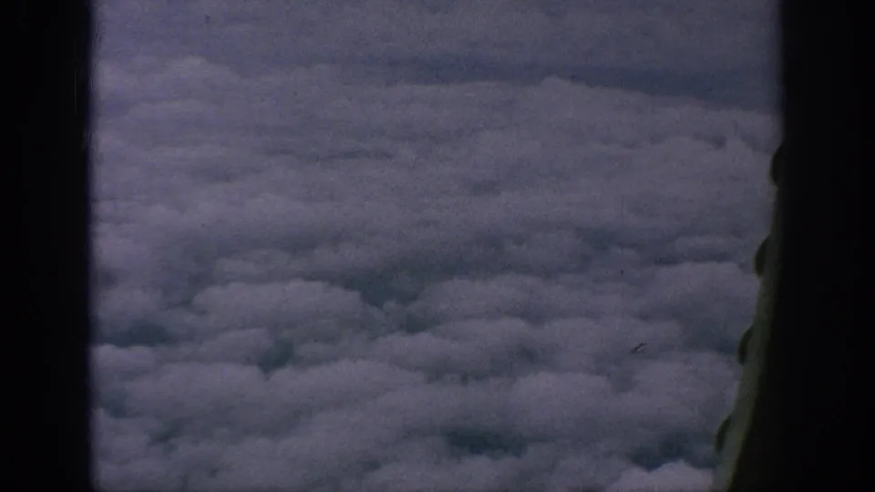1962 8mm home-movie frame looking from an aircraft window over dense white and gray cloud cover.