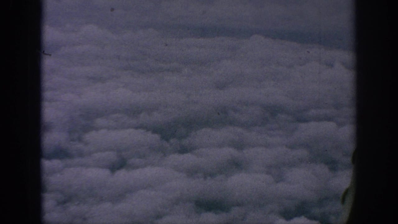 Aerial cloud view from the 1962 home-movie clip, framed by dark aircraft-window or film-gate edges.