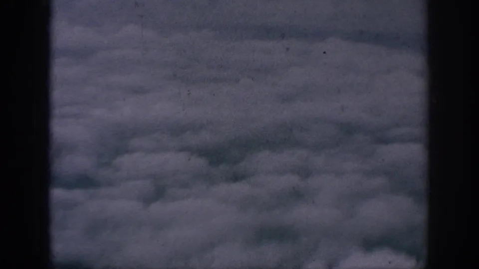 Muted 8mm aerial view over a broad cloud layer, with visible film texture and dark frame border.