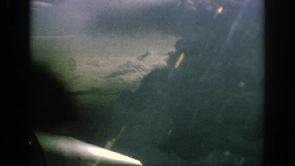 Final 1962 aerial frame with cloud cover outside and a brief aircraft wing or interior edge near the window.