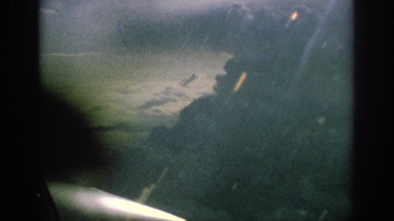 1962 Anaheim home-movie frame showing a propeller aircraft view through a window with cloud and haze beyond.