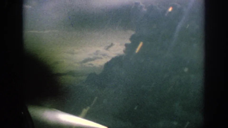 1962 Anaheim home-movie frame showing a propeller aircraft view through a window with cloud and haze beyond.