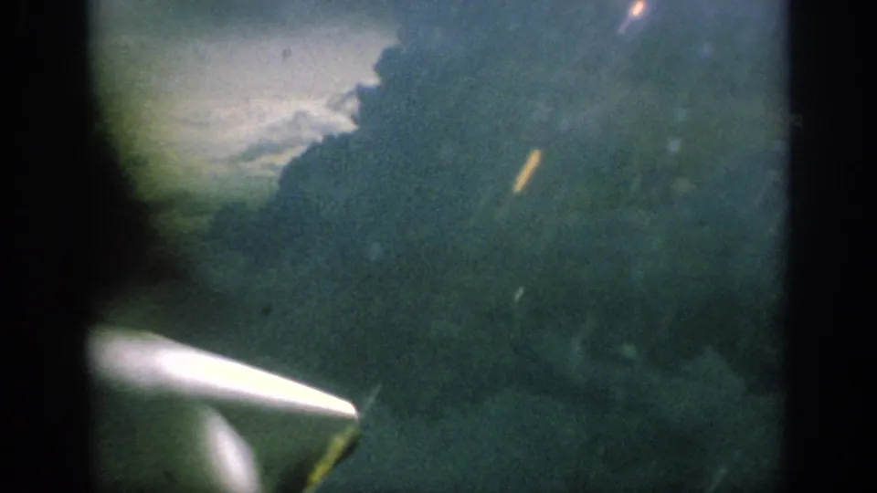 1962 Anaheim 8mm frame showing the aircraft propeller below a cloudy, green-blue passenger-window view.