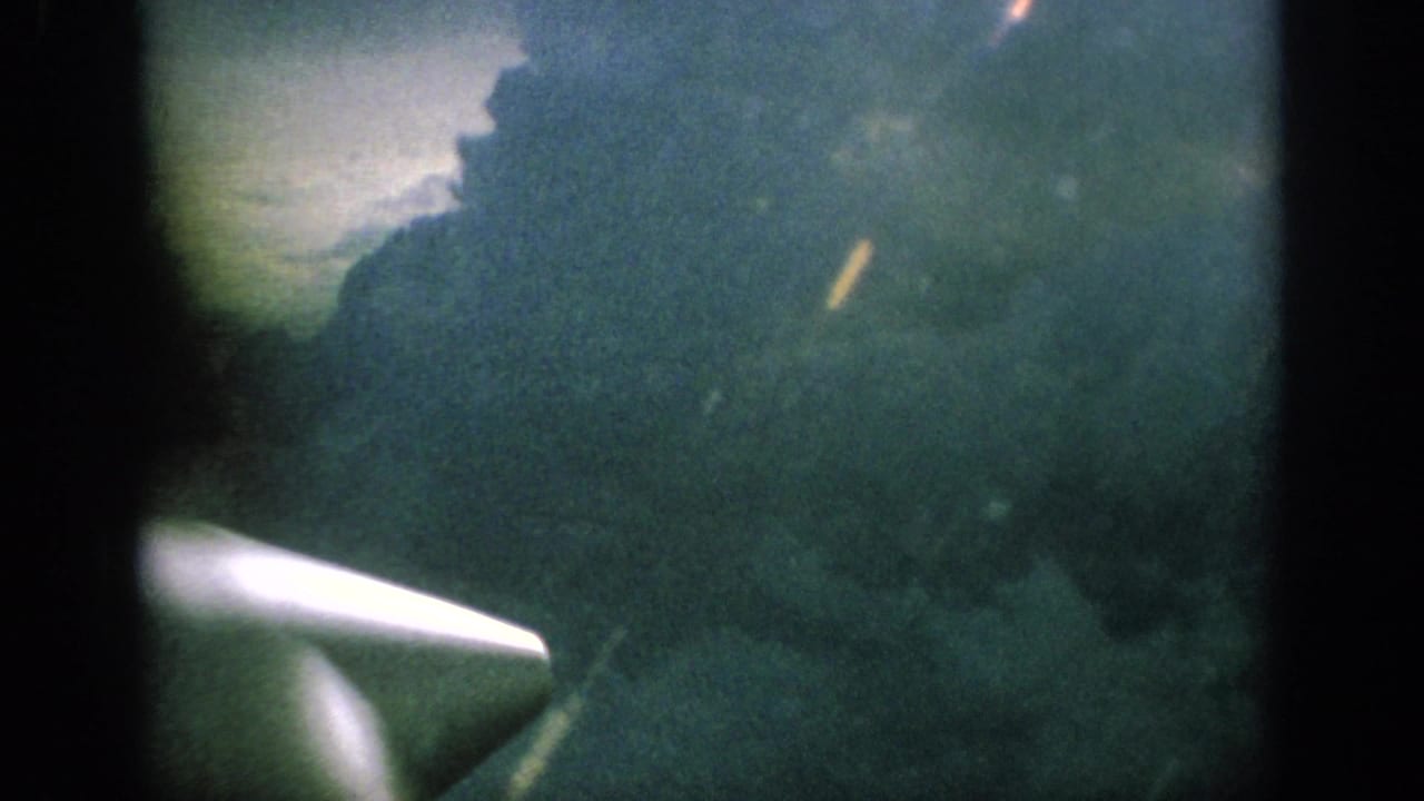 1962 8mm home-movie view from an airplane window, showing dark clouds and a white aircraft propeller or wingtip at lower left.