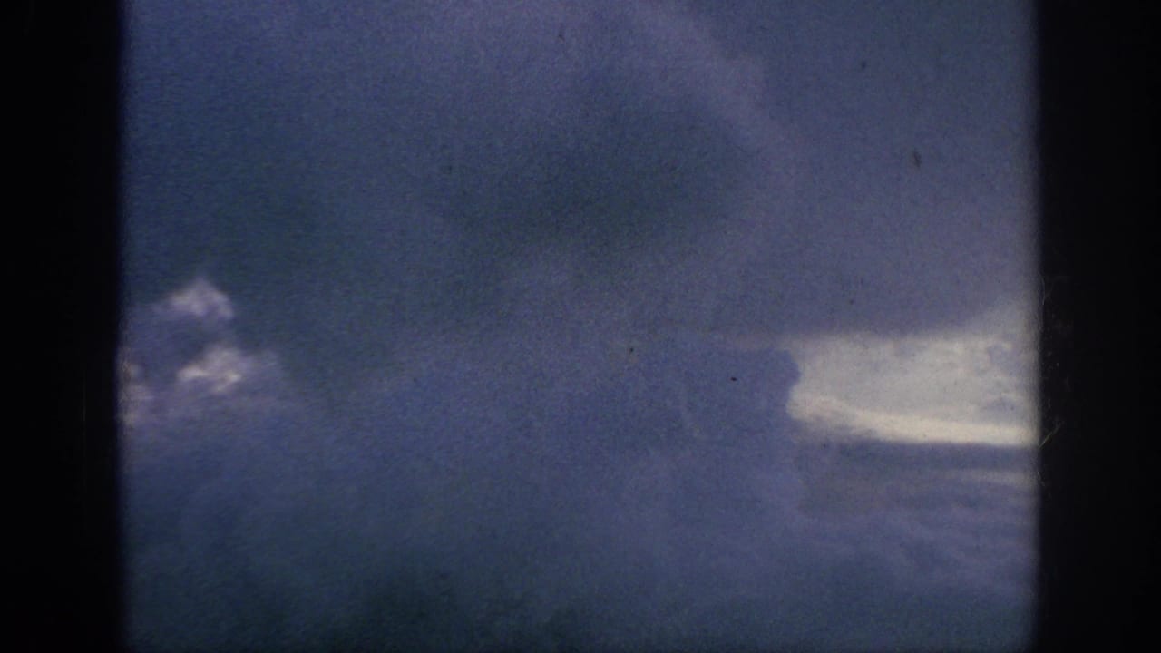 Stormy clouds and a pale sky break framed by dark vertical window edges.