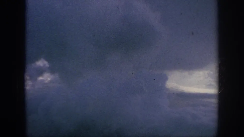 1962 8mm aerial view of storm clouds and a pale break in the sky, filmed through dark window framing.