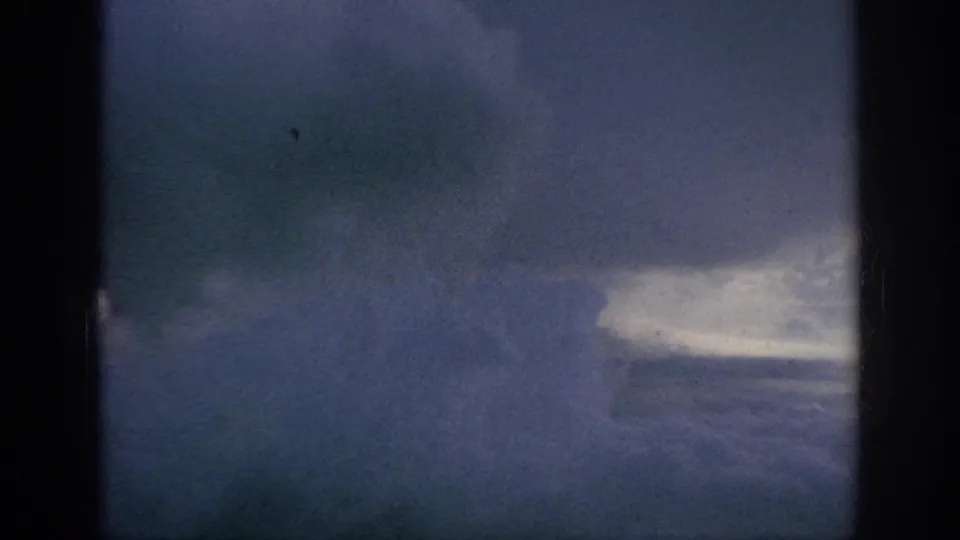 1962 8mm home-movie frame showing a hazy blue cloud field and bright cloud band through aircraft-window edges.