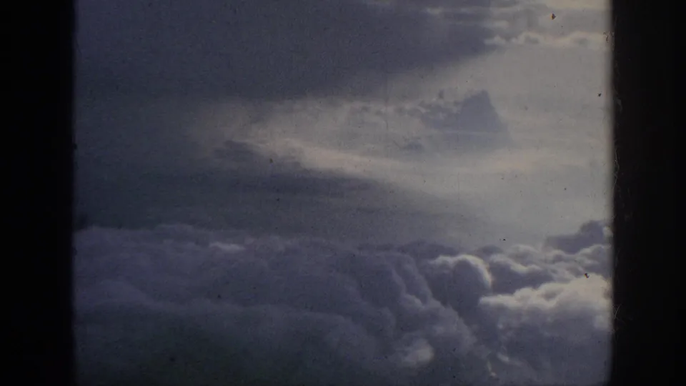 1962 8mm aerial cloud view with layered gray-white clouds, subdued sky, film grain, and dark framing at the sides.