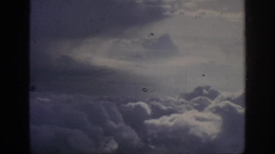 1962 home-movie aerial view of clouds from a passenger window, with visible grain, dust specks, and color fading.