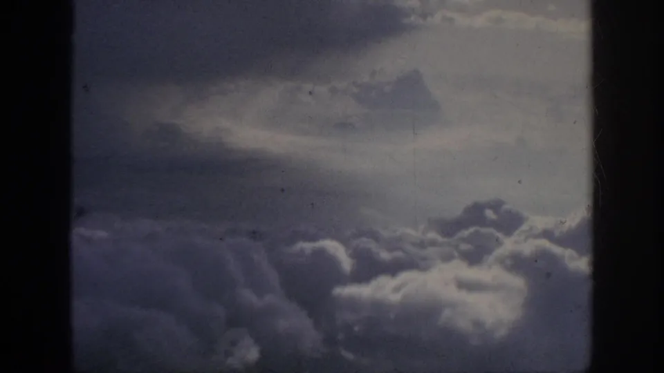 Faded 8mm airplane-window view of dense clouds and muted sky, with dark frame borders and visible film texture.