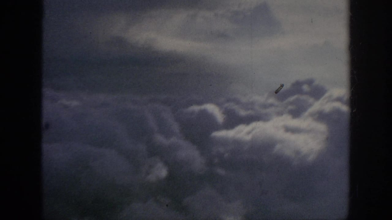 1962 8mm home-movie view from above billowing clouds, with dark frame edges, muted color, and film dust visible.