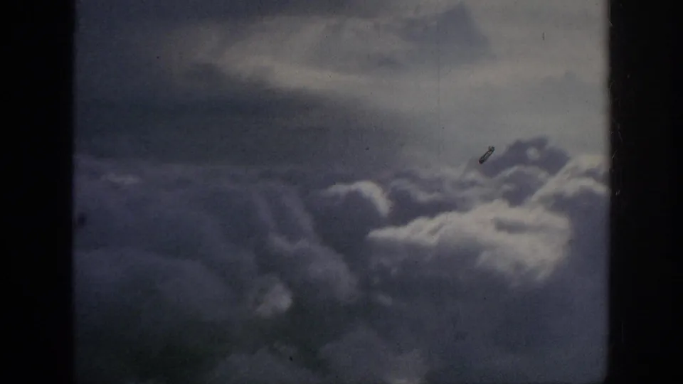 1962 8mm home-movie view from above billowing clouds, with dark frame edges, muted color, and film dust visible.