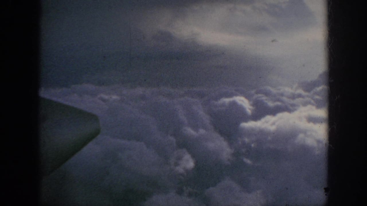 A wing or aircraft structure enters the frame over layered clouds in this 1962 8mm aerial home-movie view.