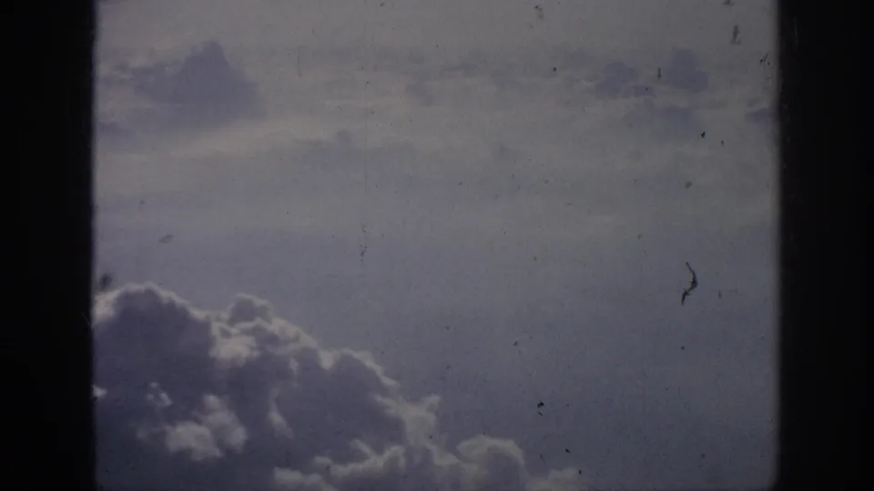 Muted 8mm footage shows cloud formations and hazy daylight from an aircraft above the weather layer.