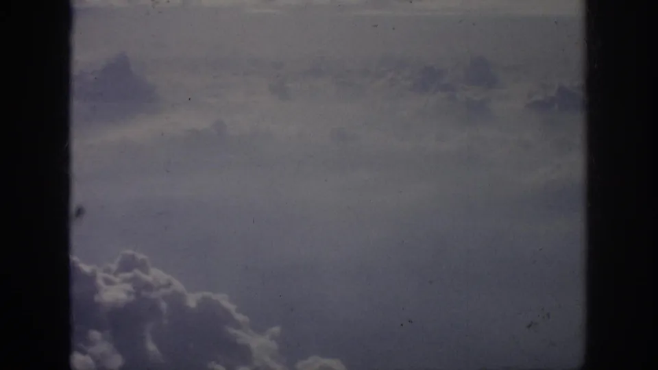 A broad cloud layer fills the frame beneath a hazy sky, rendered with visible 8mm grain and faded color.