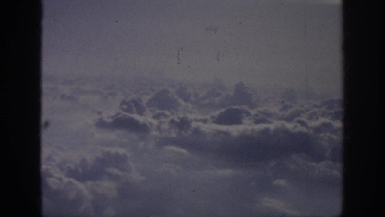 Soft gray-white clouds below a hazy sky, framed by airplane window edges.