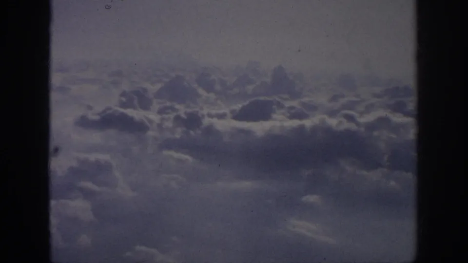 Muted 8mm frame of cloud tops from an aircraft passenger viewpoint, consistent with the 1962 travel metadata.