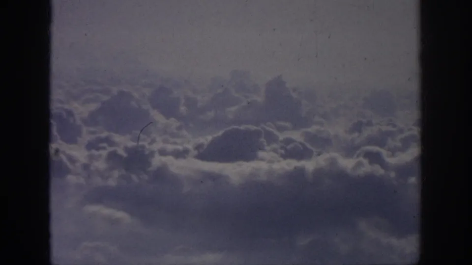 Final 8mm still showing dense cloud formations beyond the aircraft window, with visible gate edges and film texture.