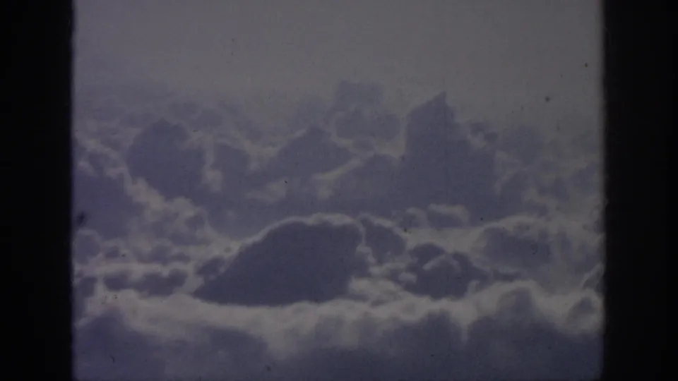 1962 8mm home-movie footage frame showing a broad cloud field from above, softened by age, exposure, and film grain.