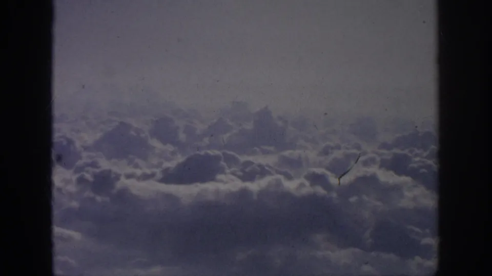 Clouds stretch across the frame in 1962 8mm footage, with a steady airplane-window perspective and pronounced dark borders.