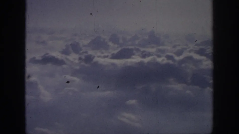 A lower contact-sheet frame shows a muted 8mm aerial cloud view, marked by grain, dust, scratches, and a horizontal frame boundary.