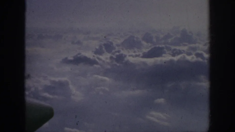 Final 1962 8mm frame of clouds seen from above, with dark vertical borders, archival wear, and a small indistinct dark shape near the bottom edge.