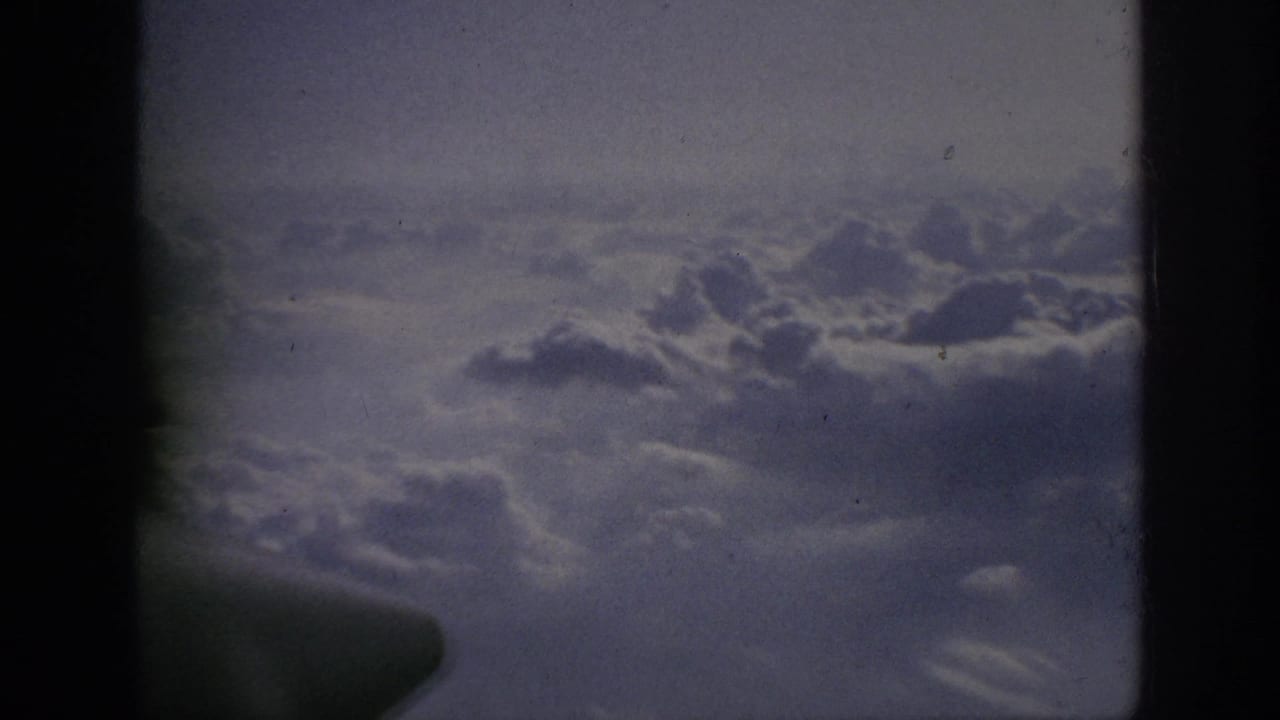 1962 home-movie frame showing clouds from an airplane window, with soft focus, grain, and dark 8mm frame edges.