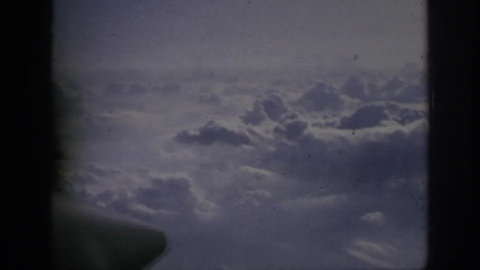 1962 home-movie frame showing clouds from an airplane window, with soft focus, grain, and dark 8mm frame edges.