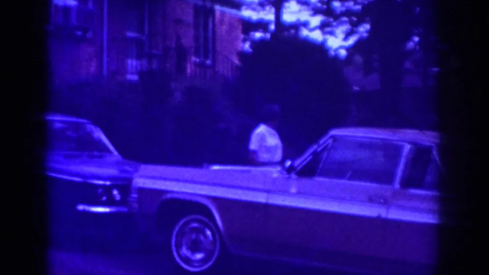 Raleigh 1962 home-movie frame with the woman near the hood of a classic sedan and another car at the curb.