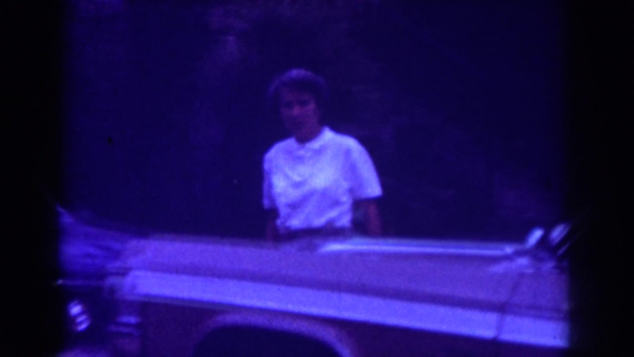 Woman faces the camera behind the side of a light-colored classic car.