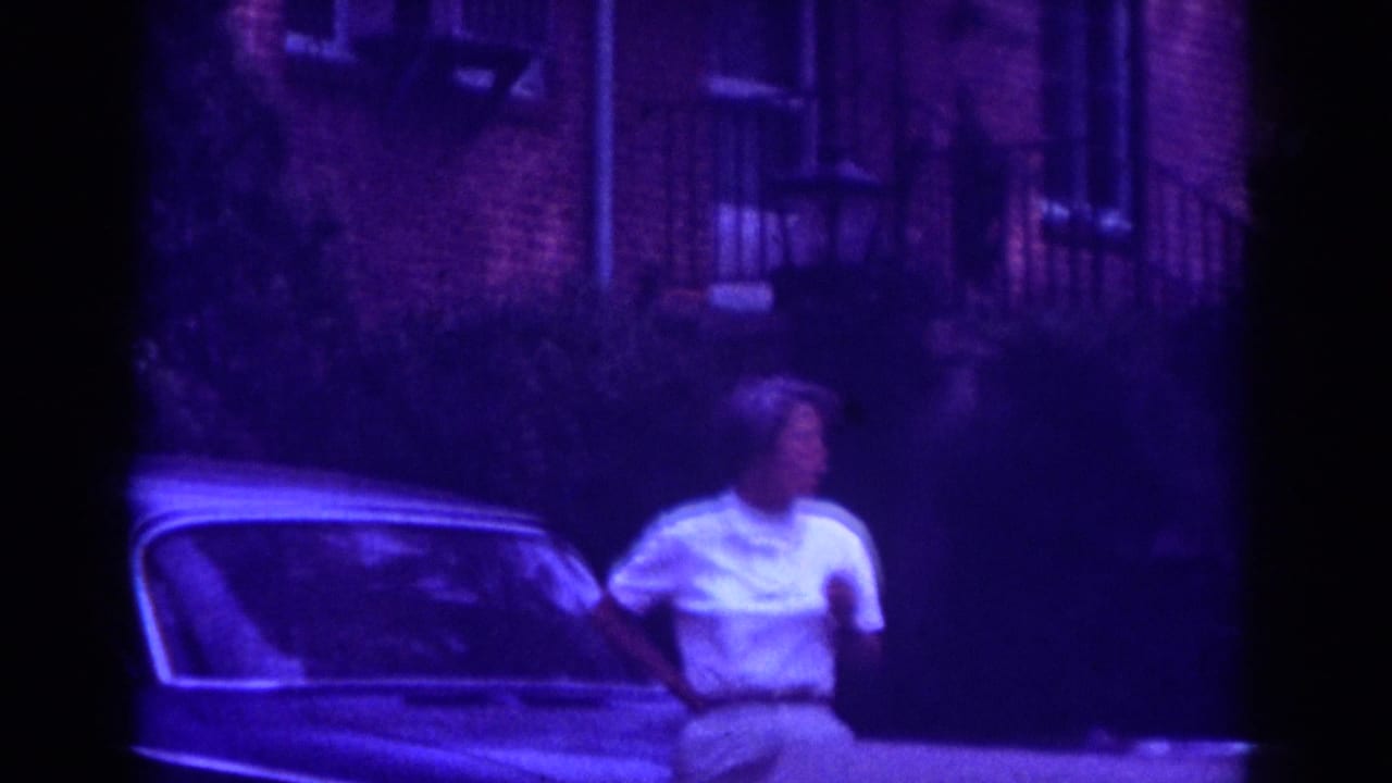 Adult woman in white shirt and khaki shorts stands near a classic car on a Raleigh residential street, 1962 metadata supported.