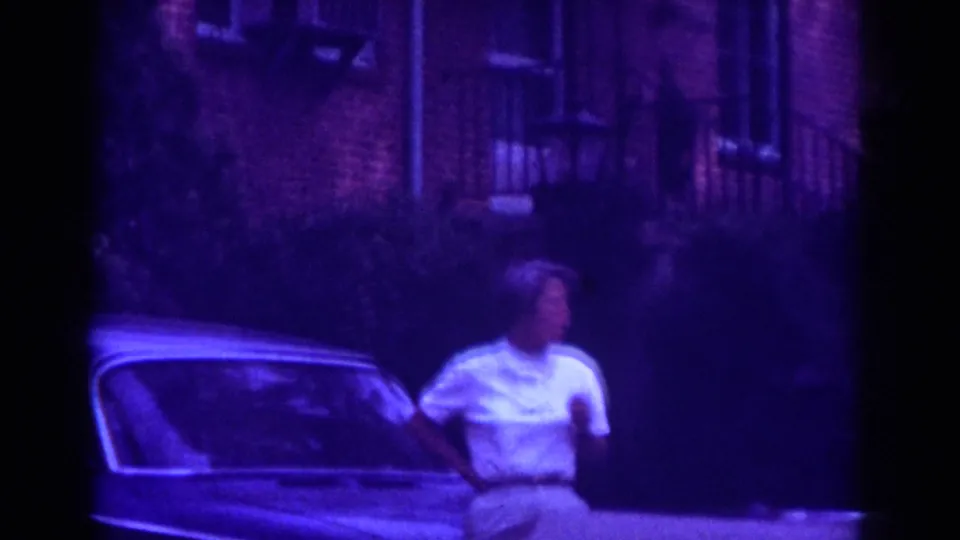 Adult woman in white shirt and khaki shorts stands near a classic car on a Raleigh residential street, 1962 metadata supported.