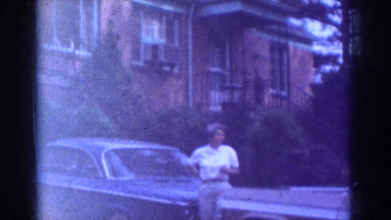 Adult woman stands near a mid-century car with brick residential buildings behind her in Raleigh, North Carolina, based on clip metadata.