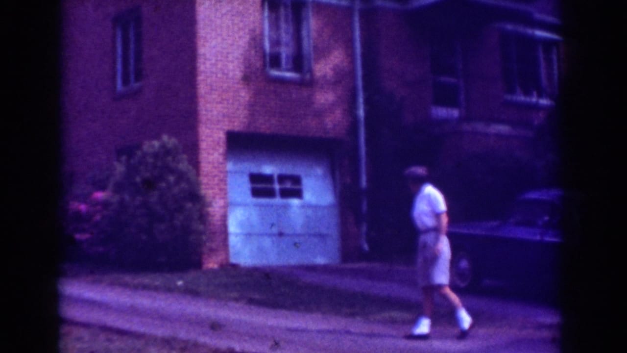 Man walking past the driveway with a white garage door and dark car behind him.