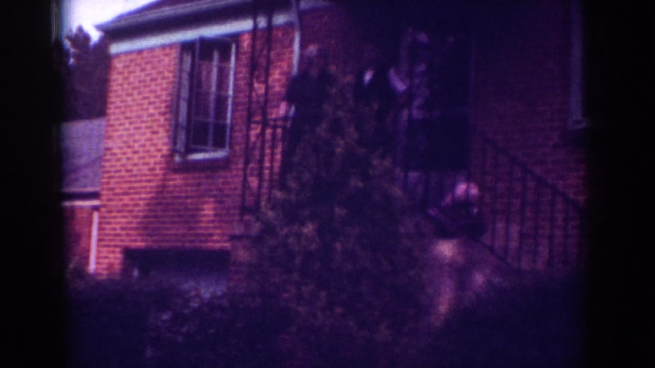 Brick house and porch with a person-shaped figure near the railing and shrubs in front.