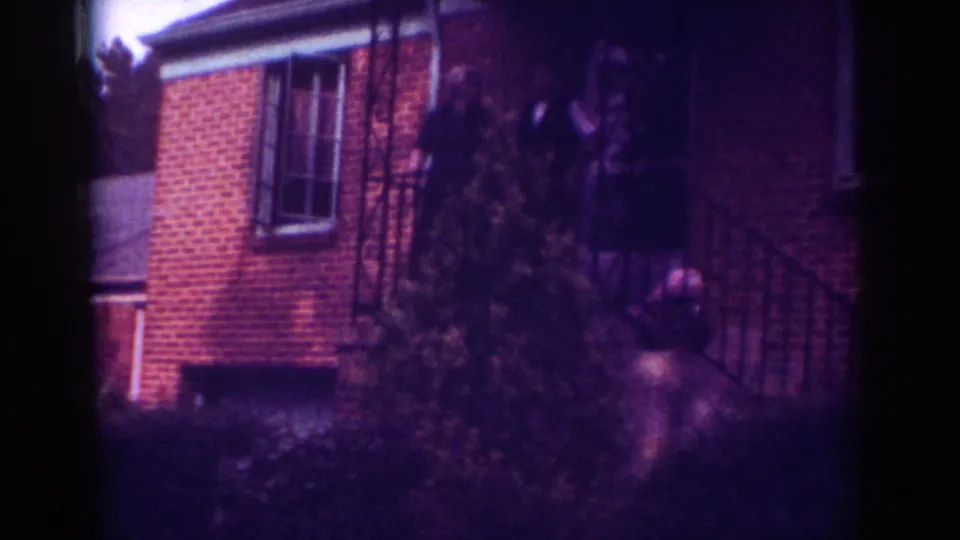 1962 Raleigh frame with a brick residential exterior, porch railing, front shrubs, and an indistinct person near the entry.