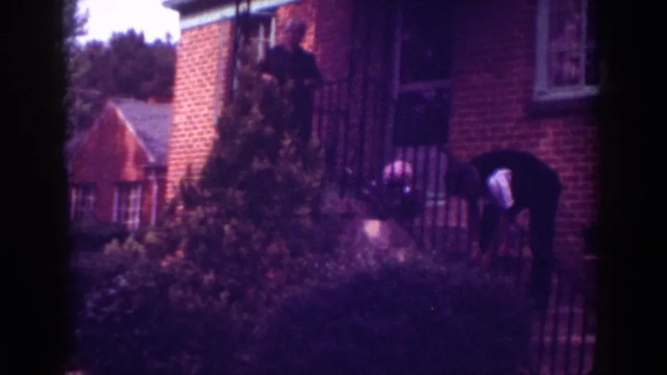 1962 Raleigh home exterior with adults near the porch steps, framed by brick walls, railings, and dense landscaping.