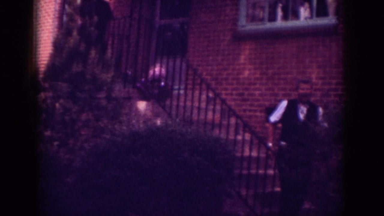 In 1962 Raleigh home-movie footage, a man stands or begins walking near exterior stairs on a brick residential facade.