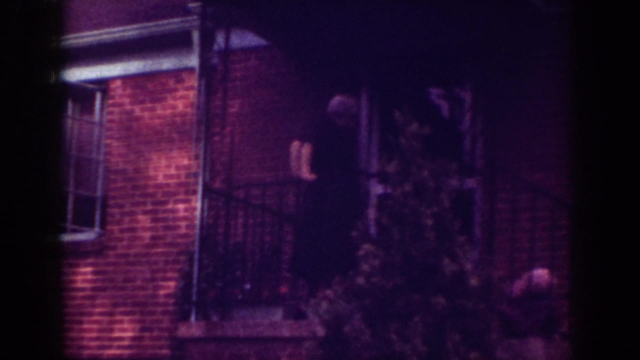 1962 Raleigh frame with an elderly man on a brick home's porch, partly obscured by foliage and railing.
