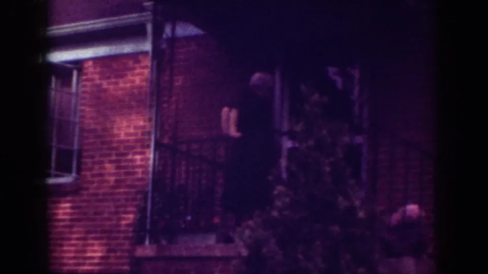 1962 Raleigh frame with an elderly man on a brick home's porch, partly obscured by foliage and railing.