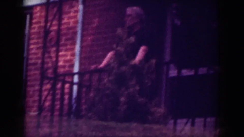 Soft-focus 1962 Raleigh frame showing an elderly man near a porch railing, with brickwork and foliage around him.
