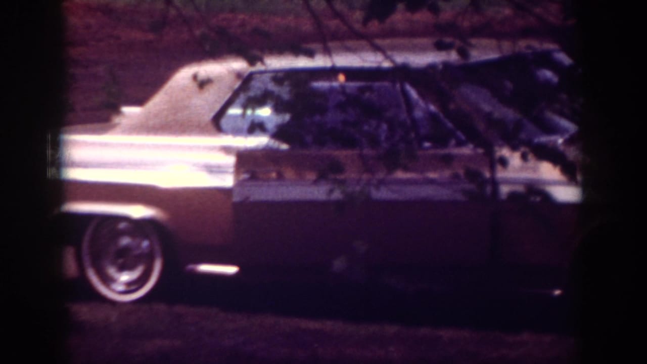 1962 Raleigh home-movie frame showing a chrome-trimmed car parked outside a brick residence.