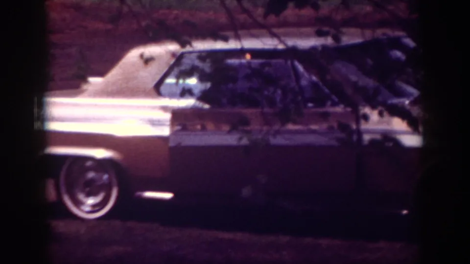 1962 Raleigh home-movie frame showing a chrome-trimmed car parked outside a brick residence.