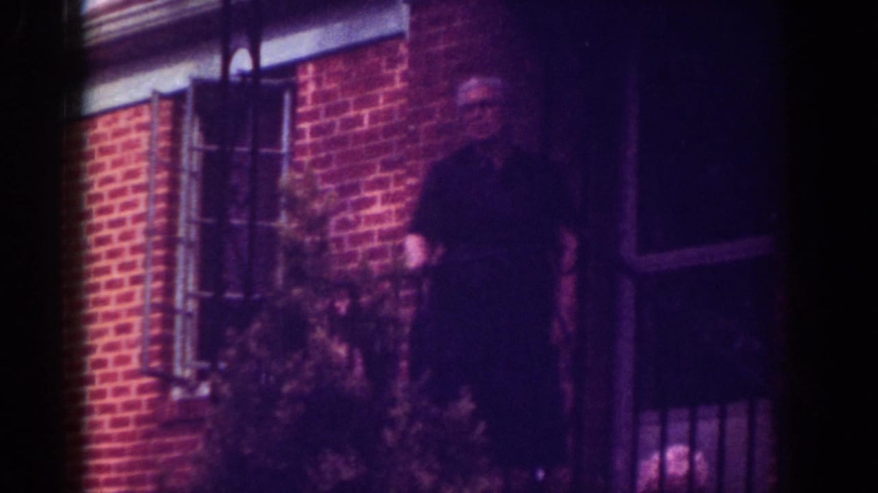 A man in a dark shirt stands by the porch of a Raleigh brick home in this 1962 home-movie frame.