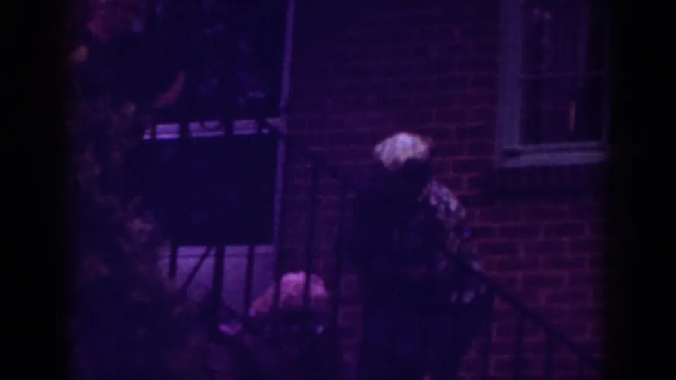 A soft-focus 1962 Raleigh frame shows the older woman bending near exterior steps, with brickwork, railing, and window behind her.