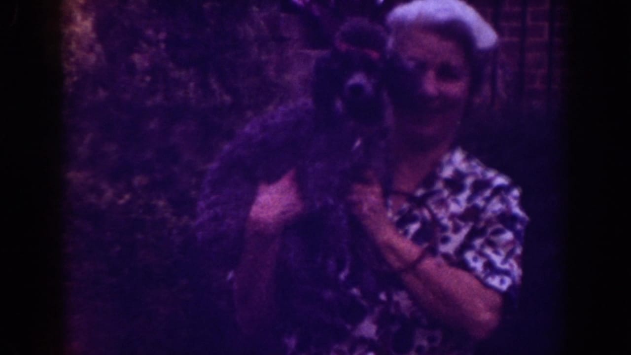 Woman smiling while holding a small dark dog near a brick wall.