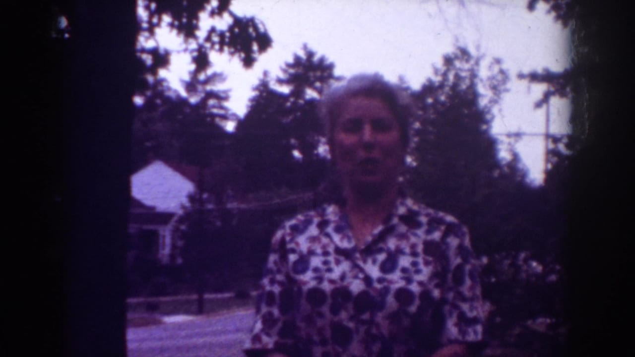 Woman faces the camera outdoors with trees and a house behind her.
