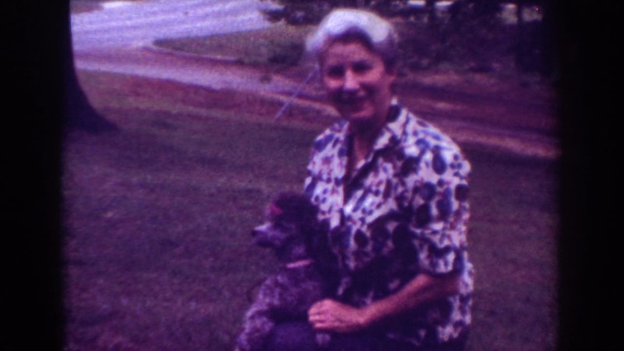 Woman smiling toward the camera while holding a small dog outdoors.